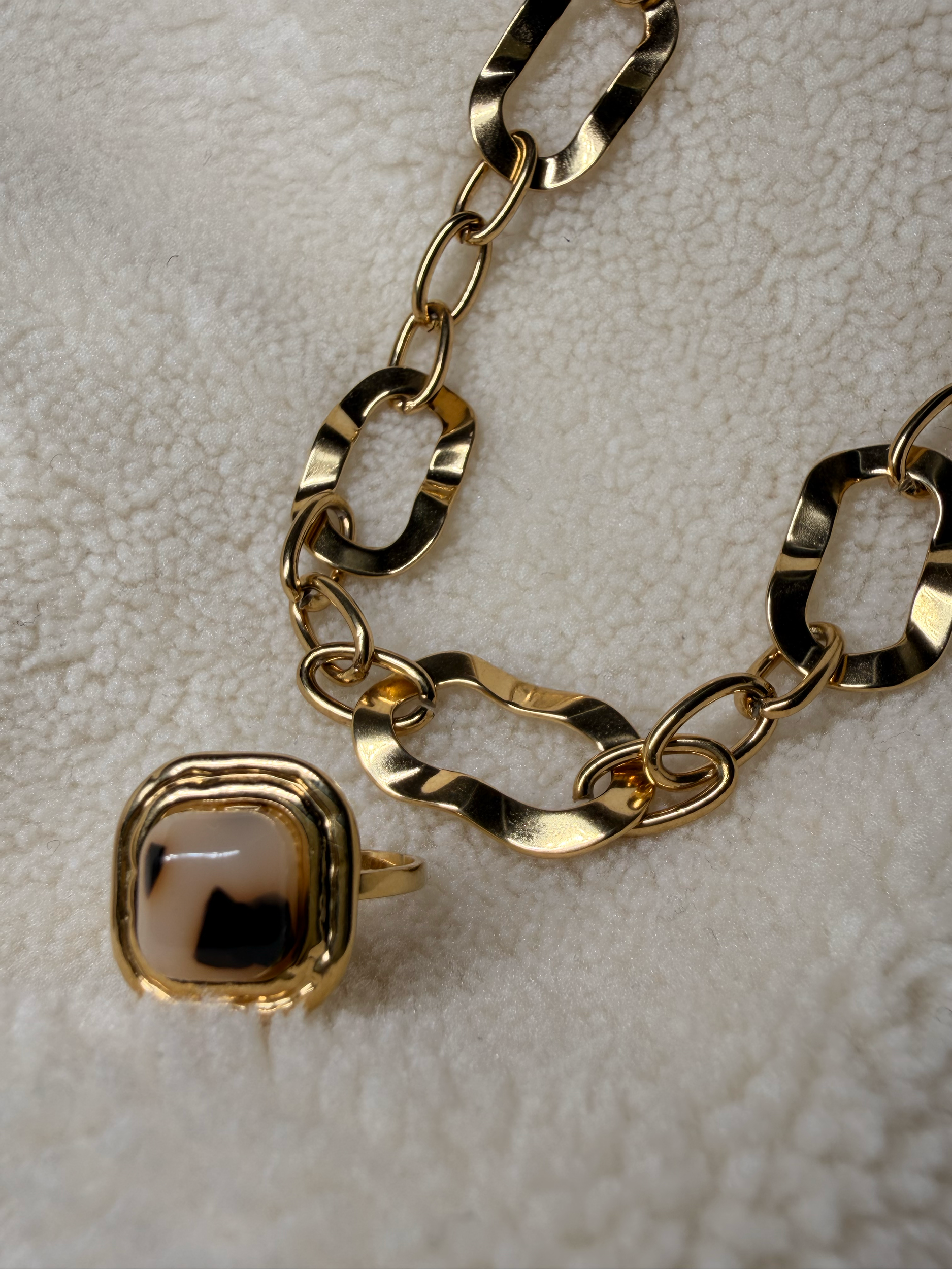 Collier doré avec de grosses maillons et un pendentif carré noir et or, posé sur une surface beige