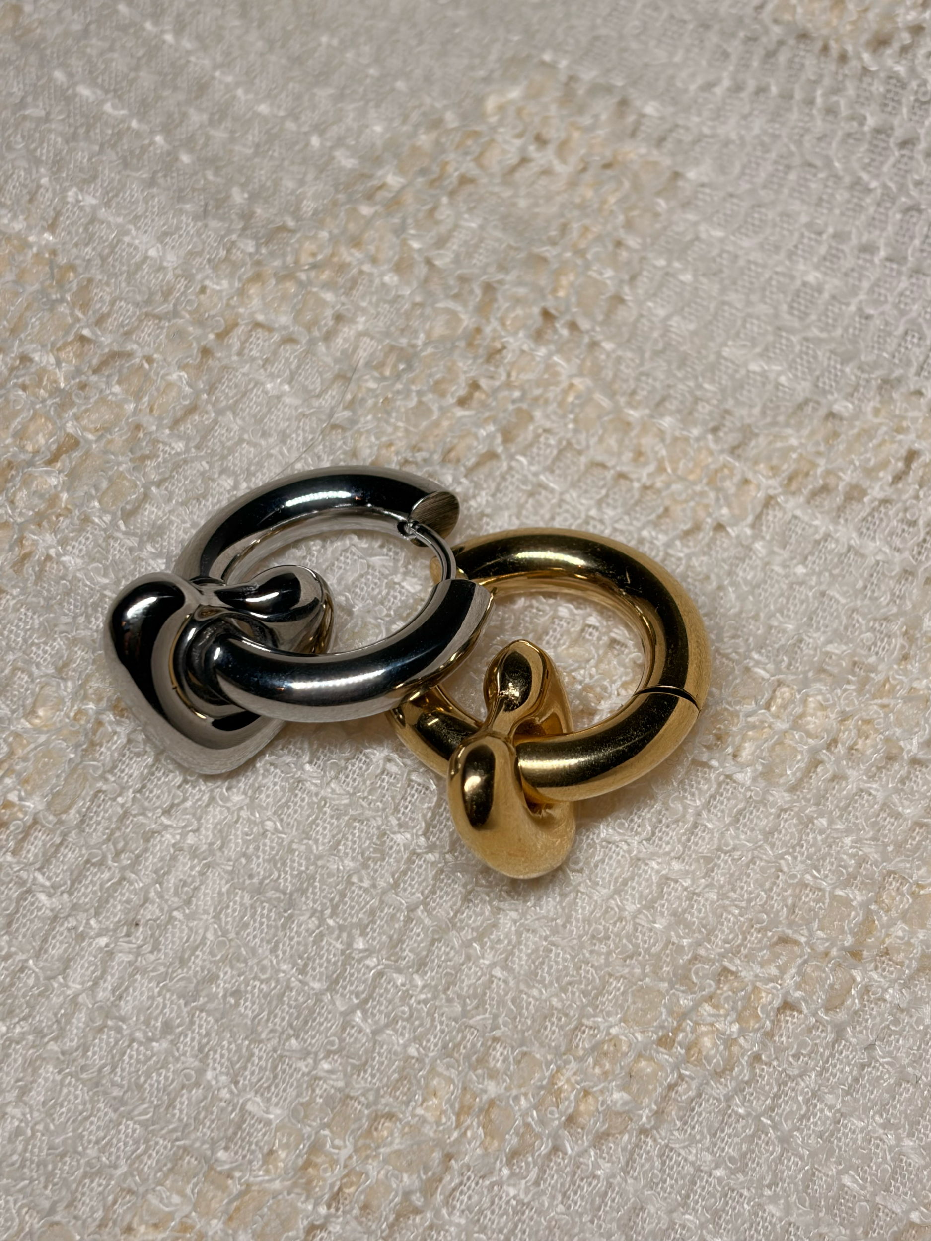 Deux anneaux métalliques, un en argent et l'autre en or, reposant sur une surface en tissu beige avec une texture claire.