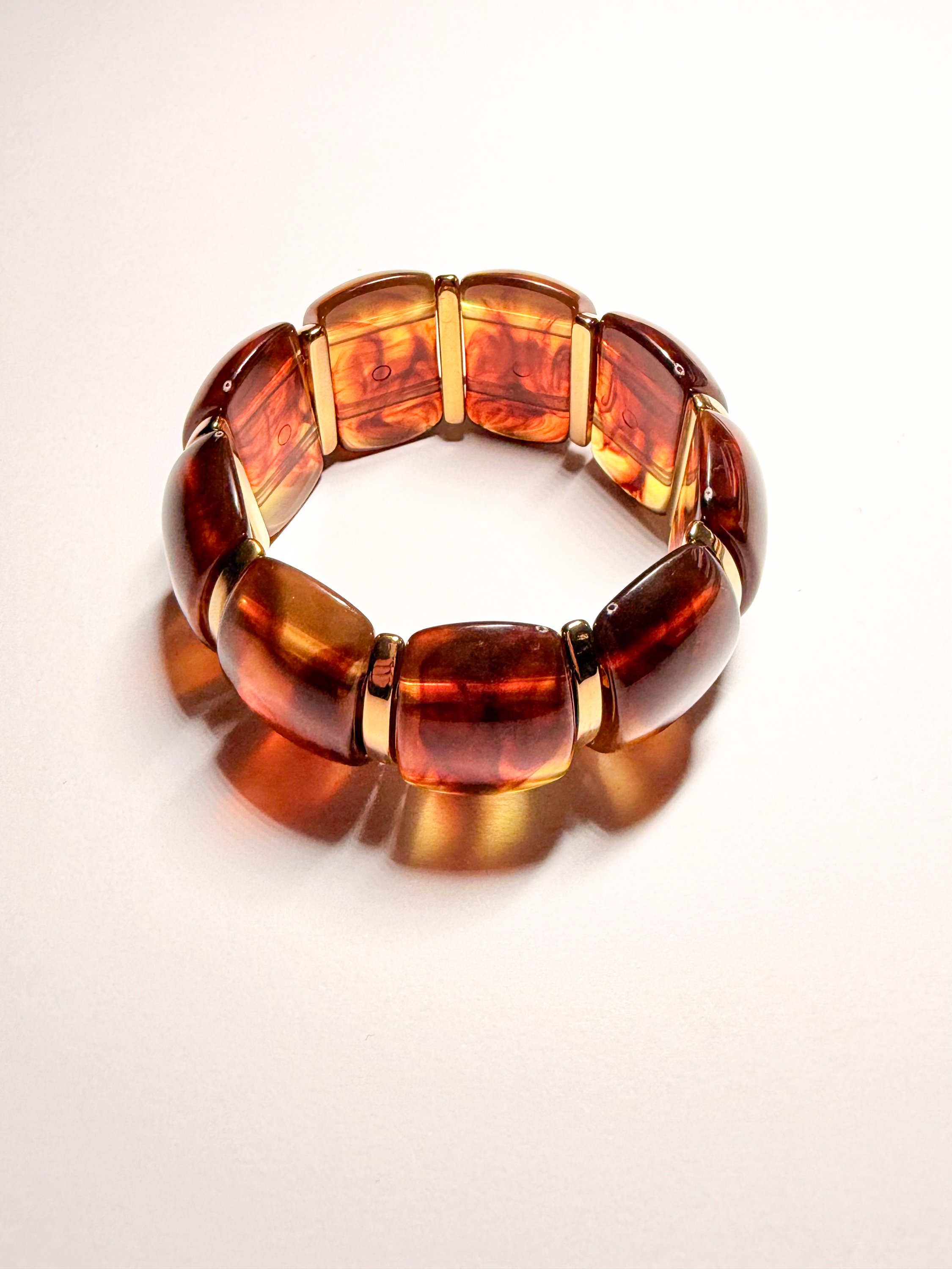 Bracelet en plastique marron avec des sections dorées, posé sur un fond blanc.