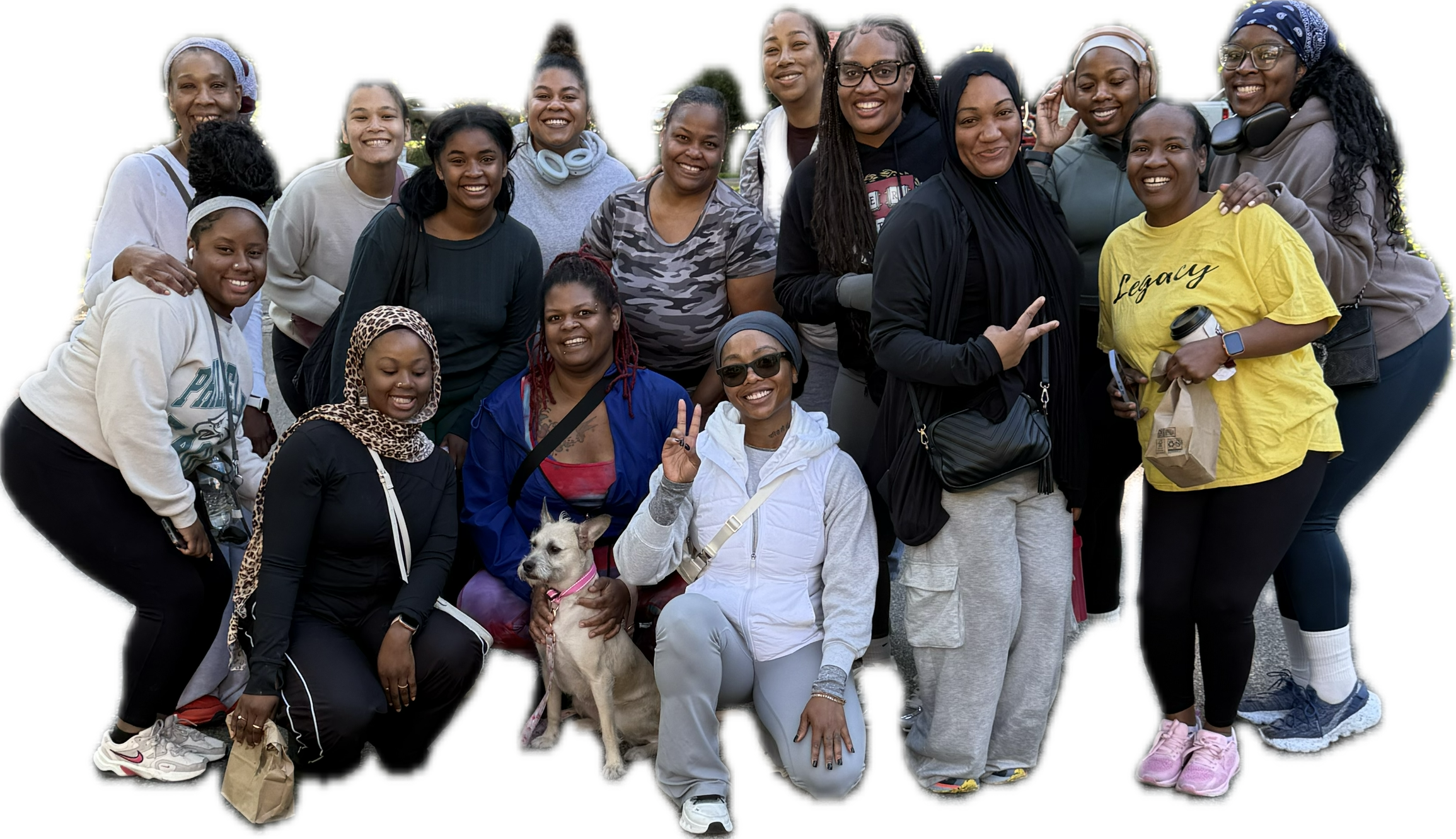 Group of diverse women smiling and posing outdoors, some making peace signs, with a dog and bags, behind a plain background.