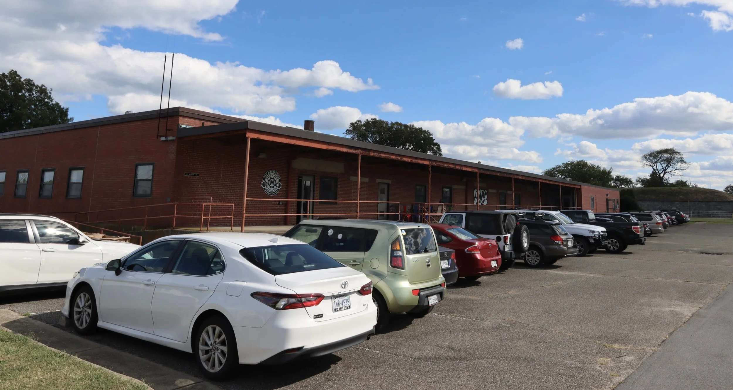 Parking lot with multiple cars parked in front of a red brick building under a partly cloudy blue sky.