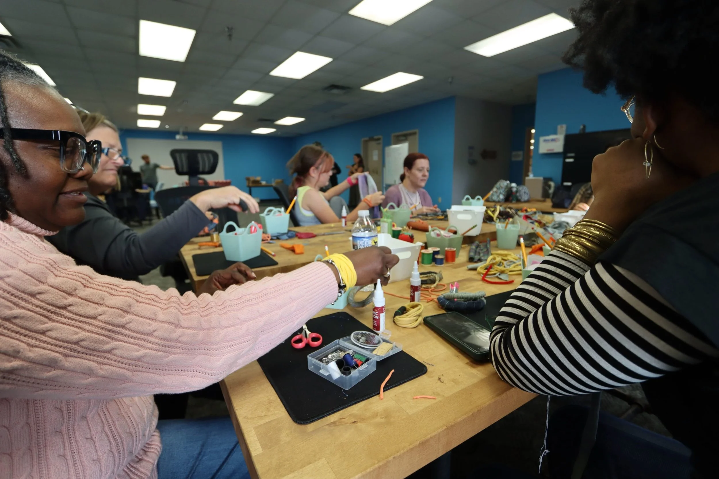 Women working on a craft project at a long table with sewing supplies in an indoor craft space.