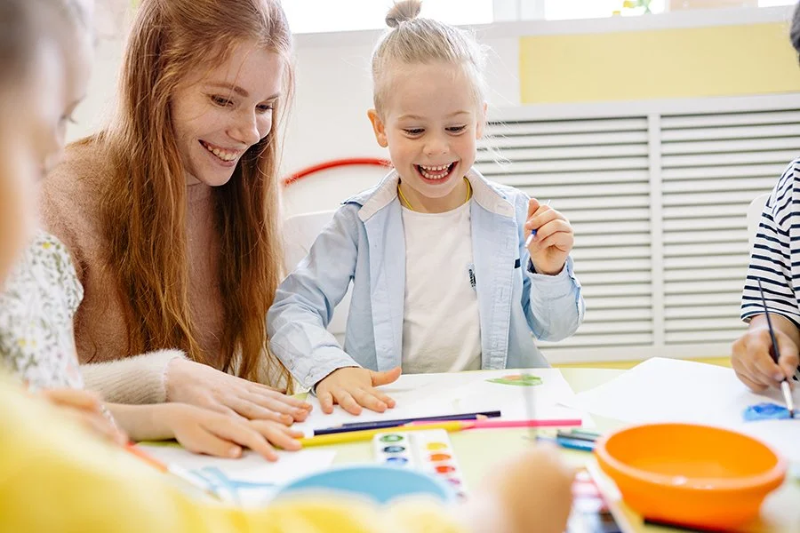 A young girl and an adult woman painting and drawing together at a table, smiling and enjoying the activity.