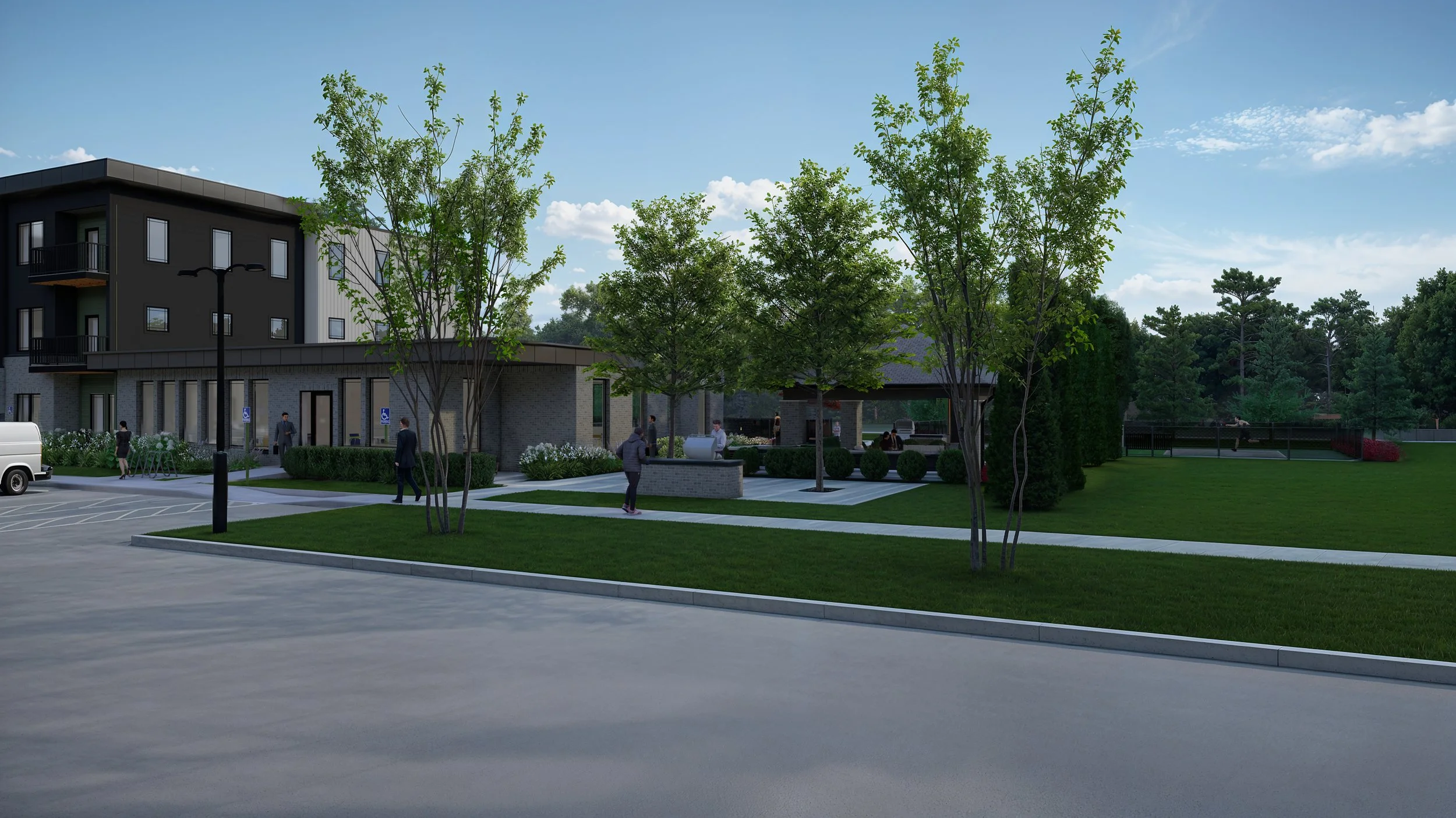 A modern residential complex with landscaped greenery, paved walkways, and people walking. There are trees, shrubs, a small pavilion, and a parking area with a few parked vehicles.