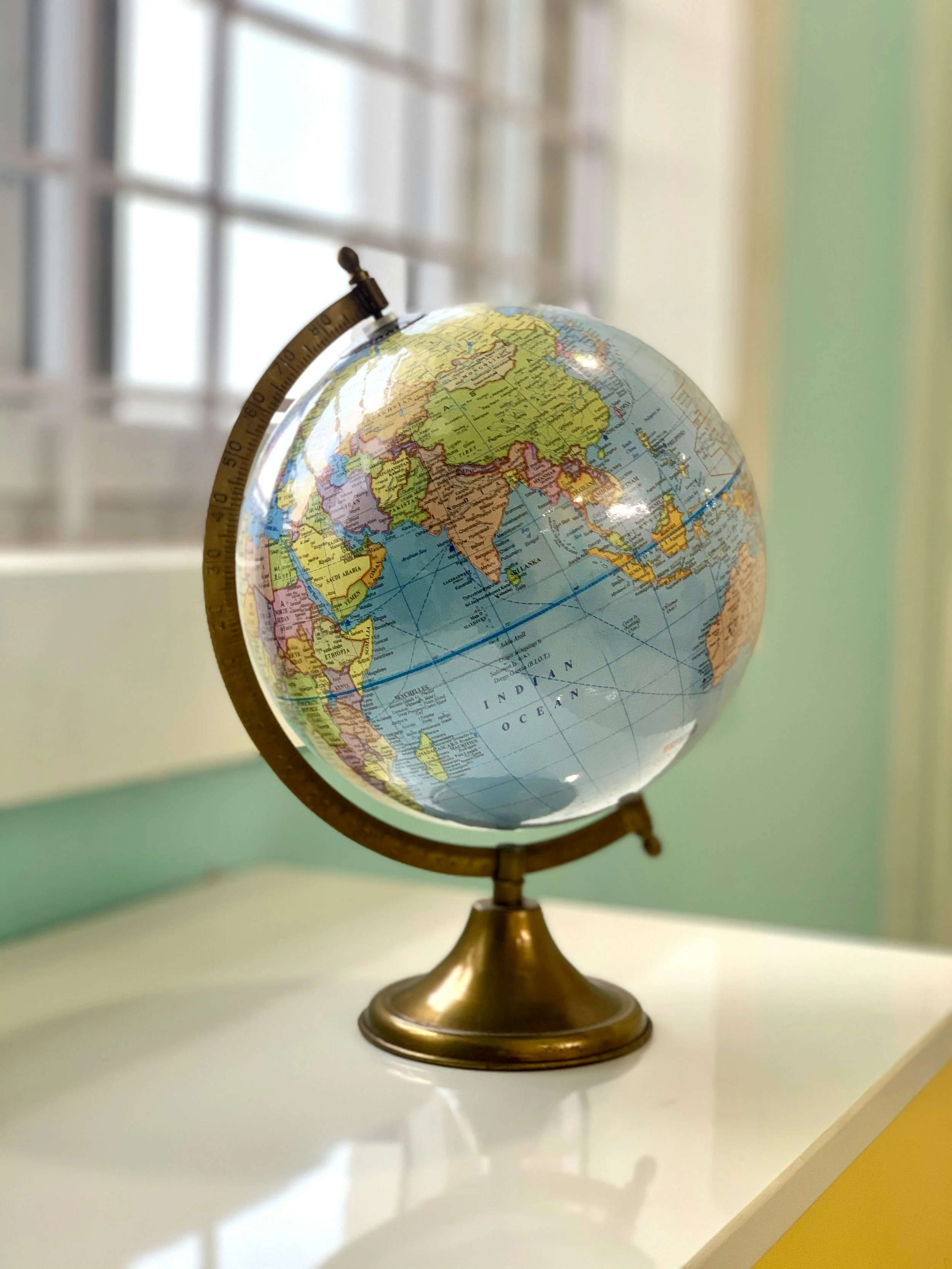 A globe showing Africa, Asia, and Oceania, placed on a white surface near a window with metal bars.