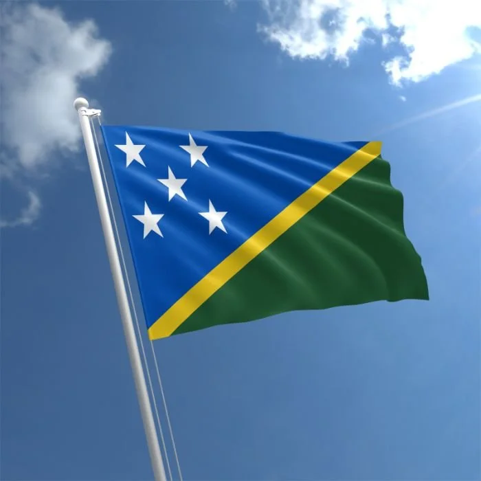 The national flag of the Solomon Islands waving in the breeze under a partly cloudy sky.