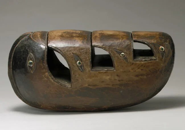 A carved wooden object resembling a stylized animal head with three openings and metal accents.
