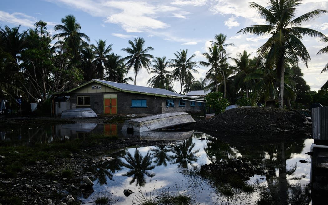 A flooded area with a house, palm trees, and an overturned boat reflecting in the water.