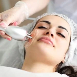 A woman receiving a facial treatment with a skincare device from a technician in a clinic.