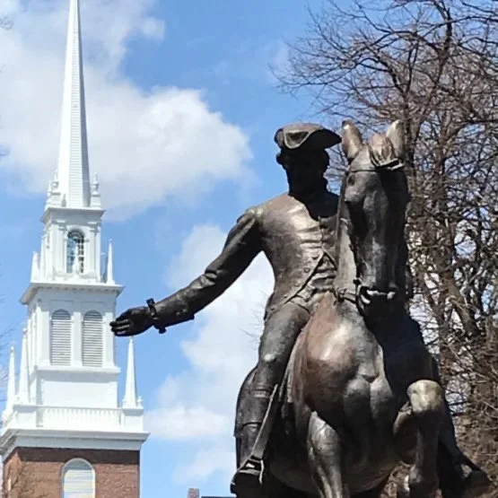 Bronze statue of a man on a horse with a church steeple and trees in the background.