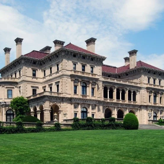 Large historic mansion with detailed architecture and a manicured lawn under a partly cloudy sky.