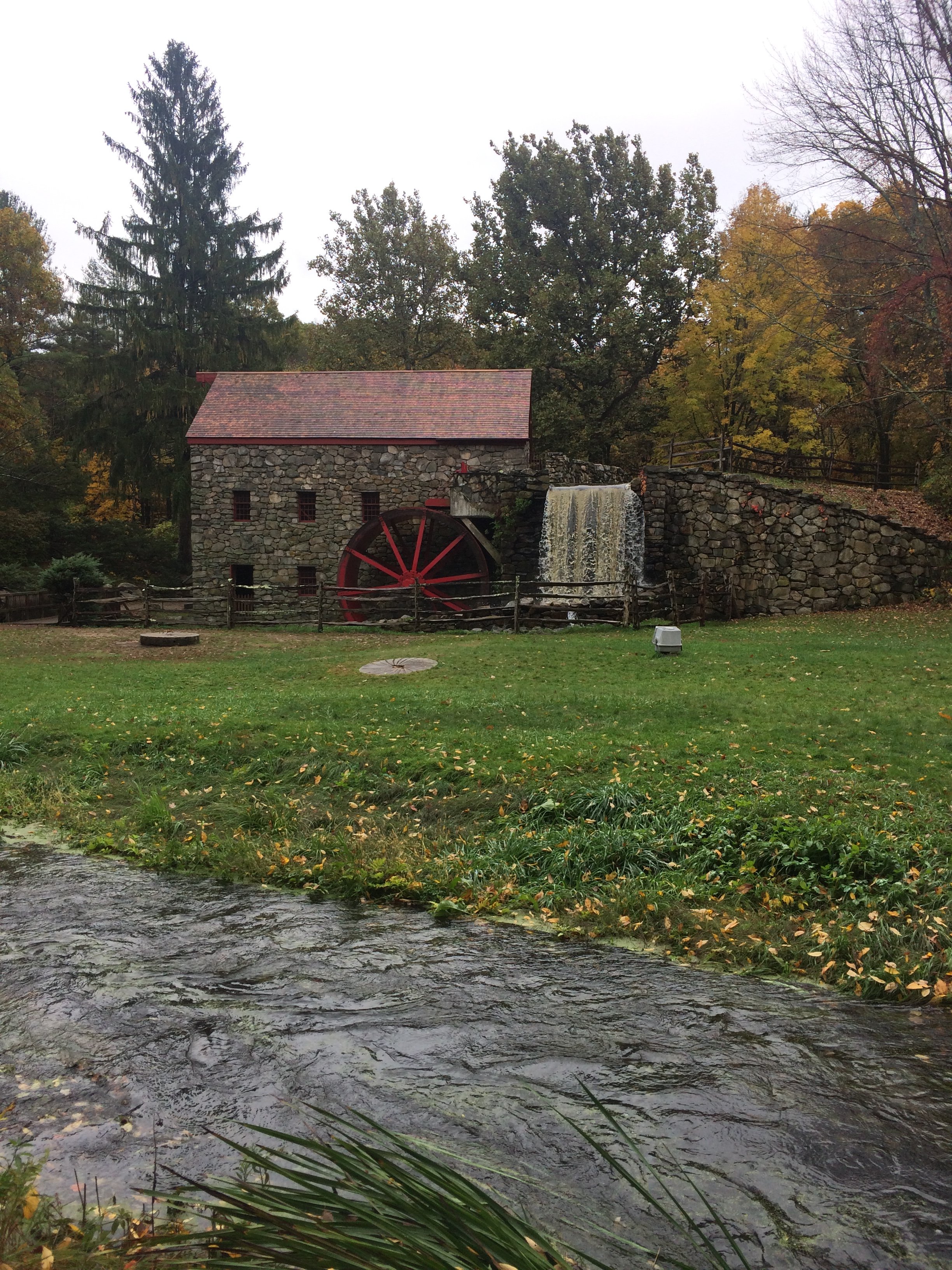 Historic stone mill and red water wheel surrounded by foliage at the Lincoln Sudbury Wayside Inn