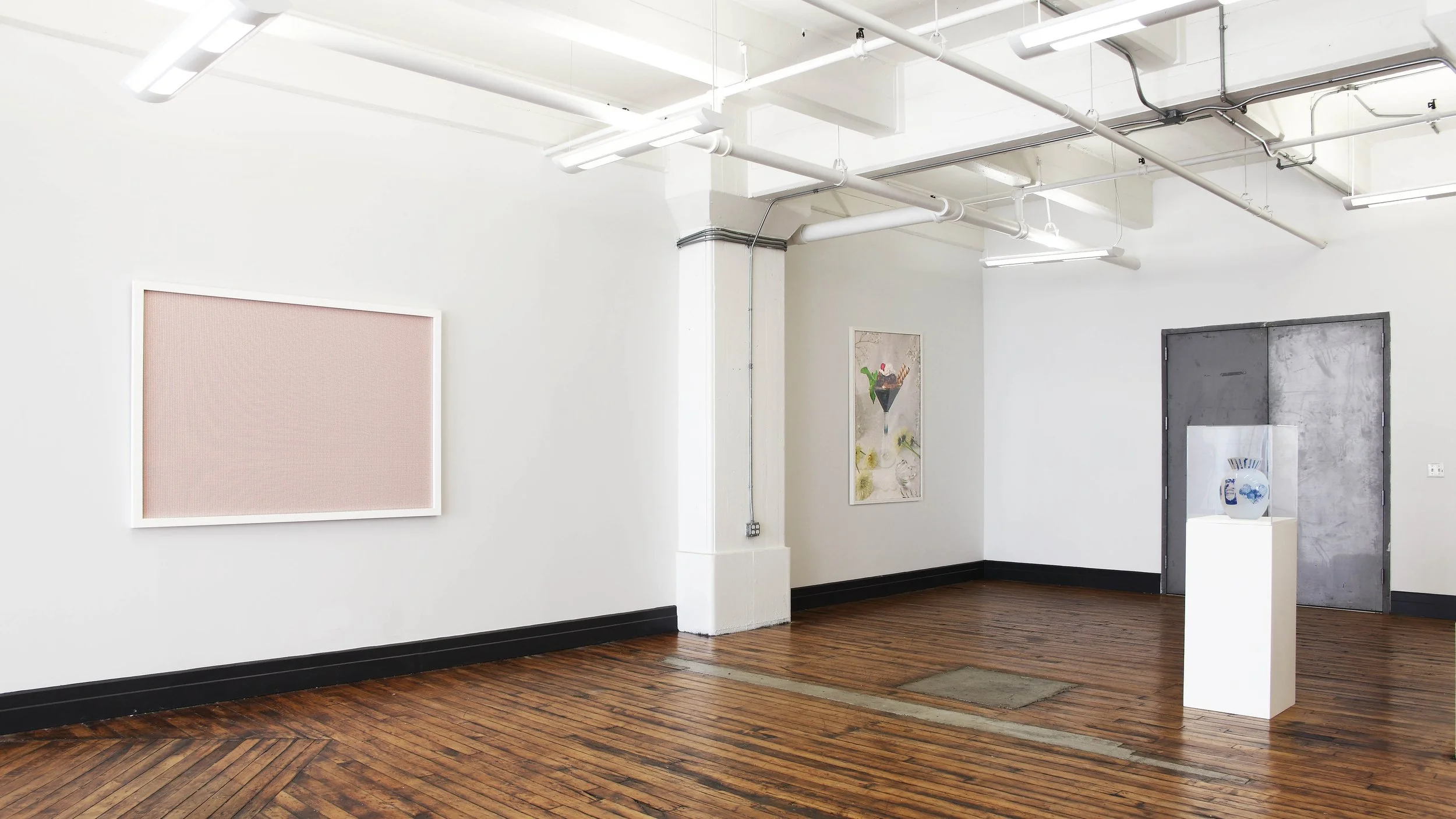 An art installation with a large framed pink print, a framed photograph of what appears to be food and a ceramic vase on a pedestal.