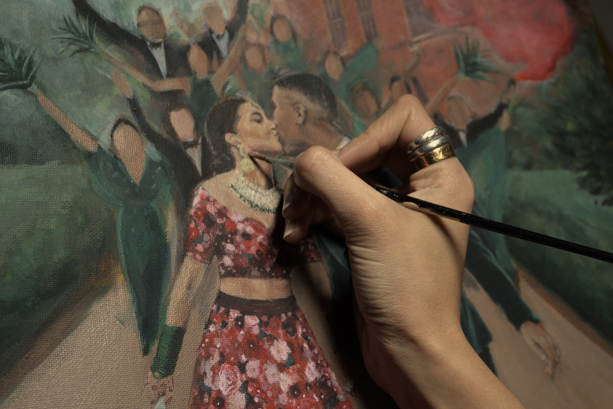 Close-up of an artist painting a romantic scene with a man and woman kissing, surrounded by other figures in formal attire, on a canvas.