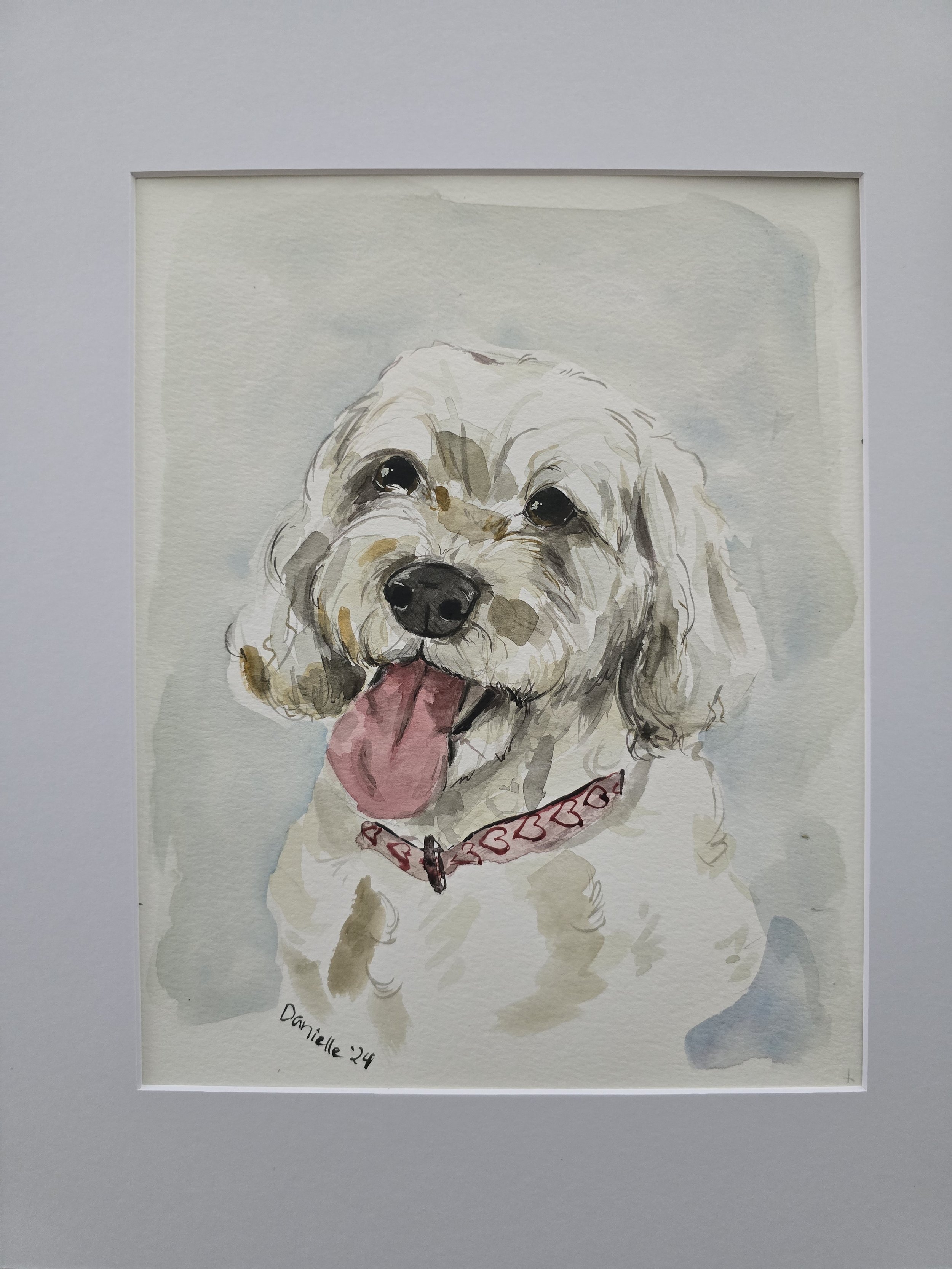 Watercolor painting of a happy dog with a pink tongue hanging out, wearing a red collar with hearts, framed in a white border.