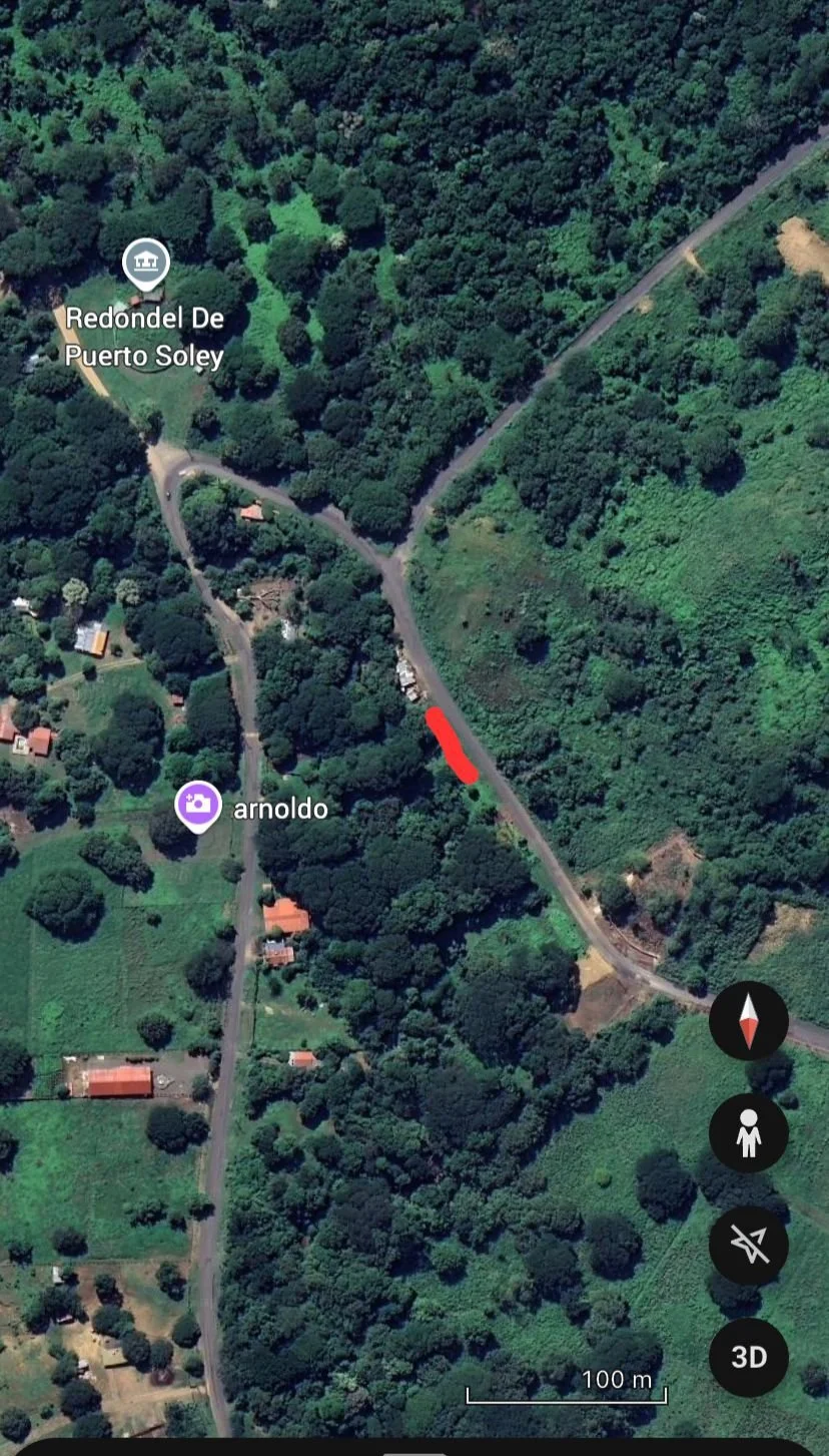 Satellite view of a green, forested area with roads and a few houses. Labels indicate 'Redondel De Puerto Soley' and 'arnoldo'. A red marker is along one of the roads.