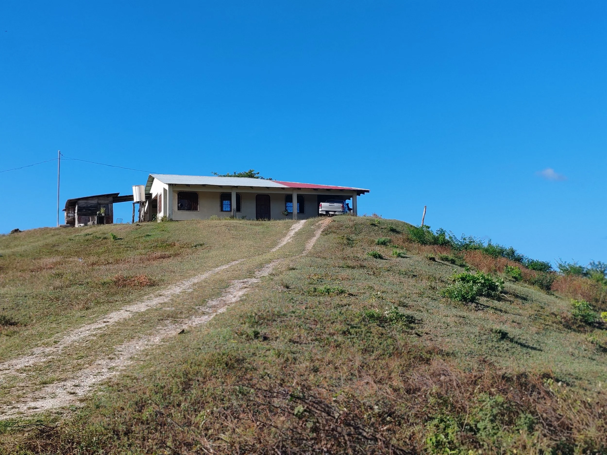 A house on top of a hill with a dirt driveway leading up to it, under a clear blue sky.