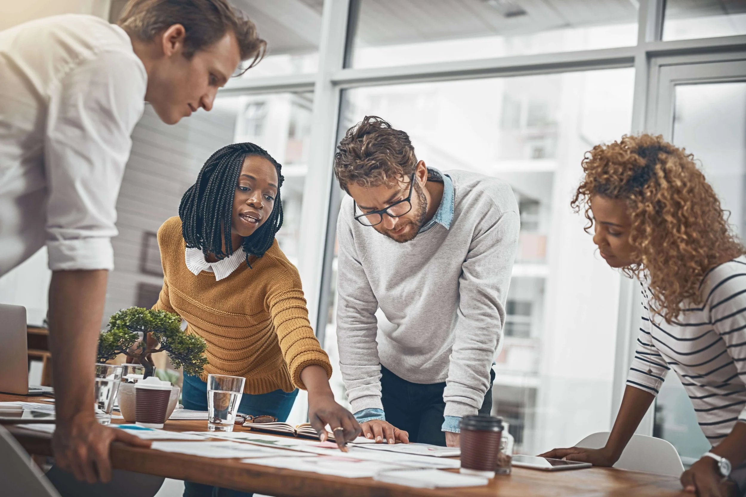 Group of five diverse people working together around a table with papers, laptop, and coffee in a modern office.