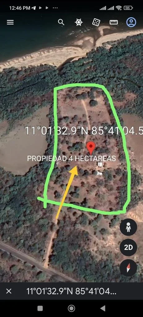 Satellite view of a 4-hectare property outlined in green near a large body of water, with a dirt road leading to it and some scattered trees and structures within the property.