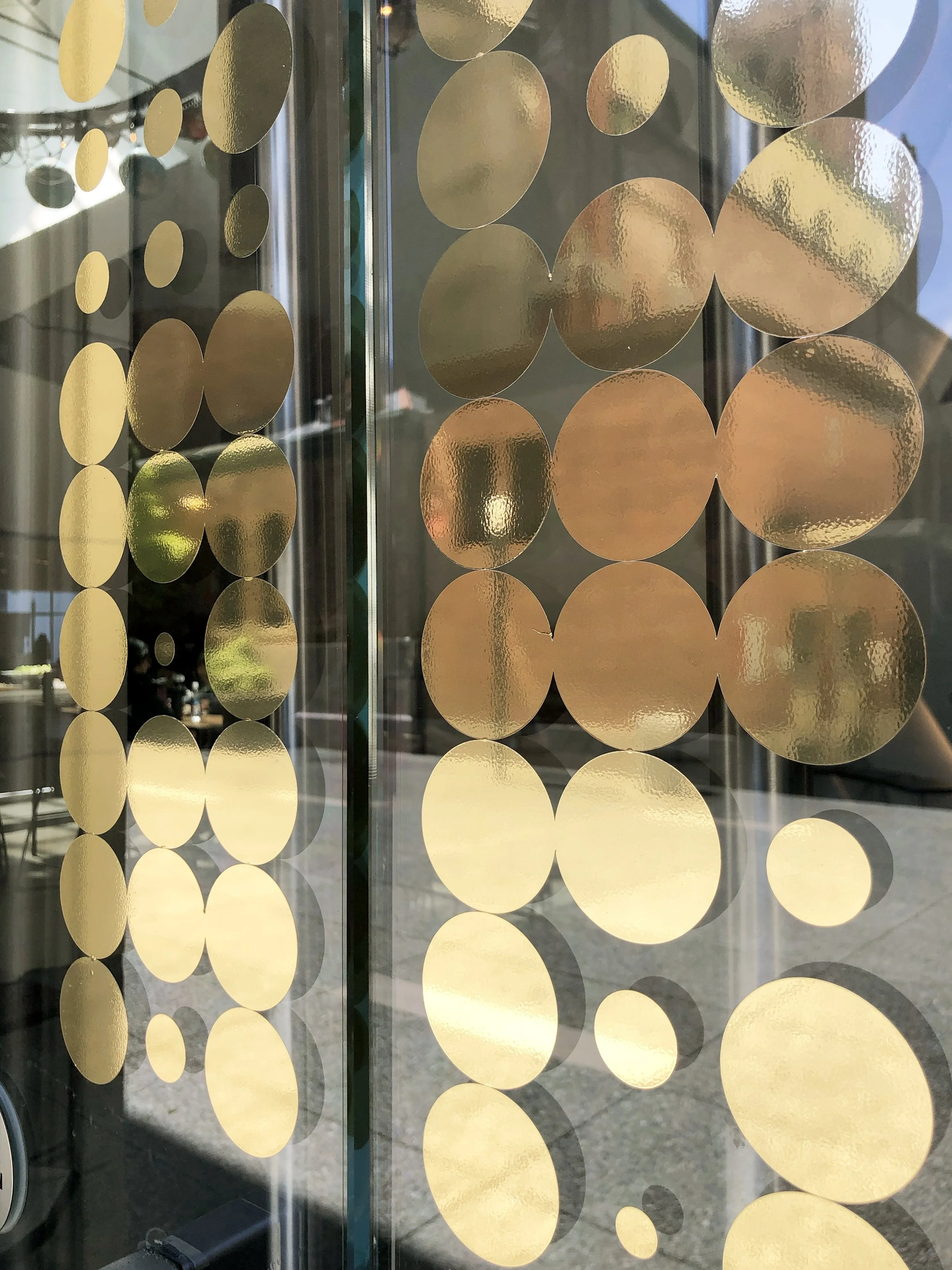 Consequent environmental graphics and wall decals: Glass door decorated with gold circular wall decals of various sizes, reflecting light and objects in the background.
