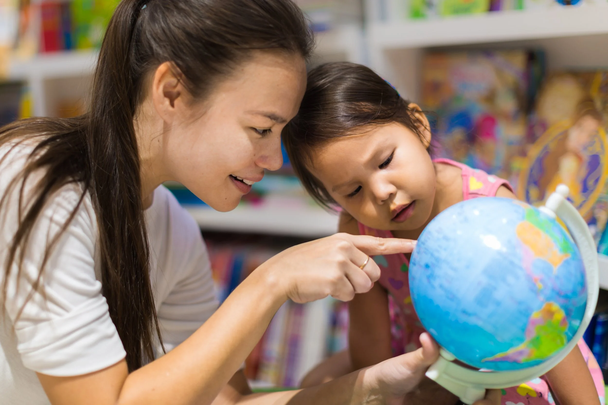 Image library for Stanford FIND: A woman and a young girl examining a globe together in a colorful classroom setting.