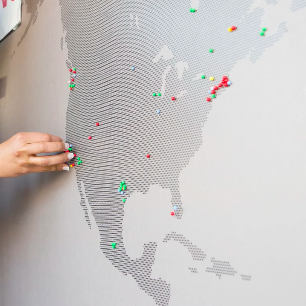 Stanford LEAD program large printed interactive map: A dotted map zoomed in on North America with colorful pushpins marking various locations of participants, and a hand placing a pin.
