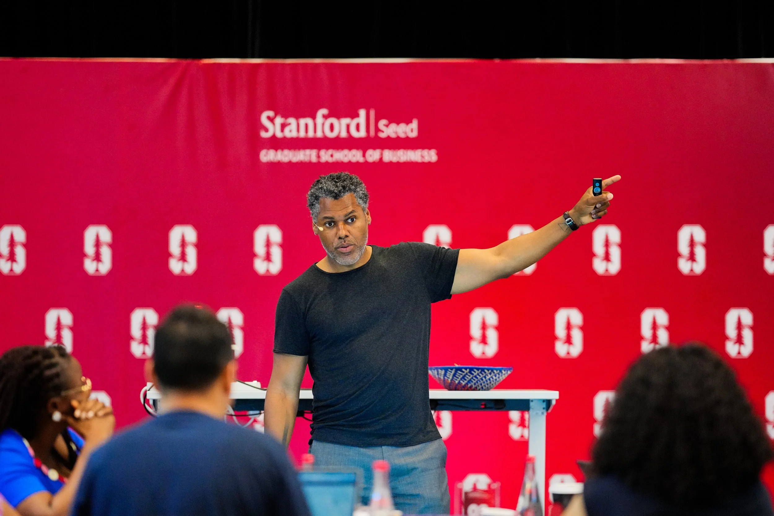 Brian  Lowery giving a presentation in front of an audience at Stanford Seed Graduate School of Business, with a red backdrop featuring the Stanford logo and text.