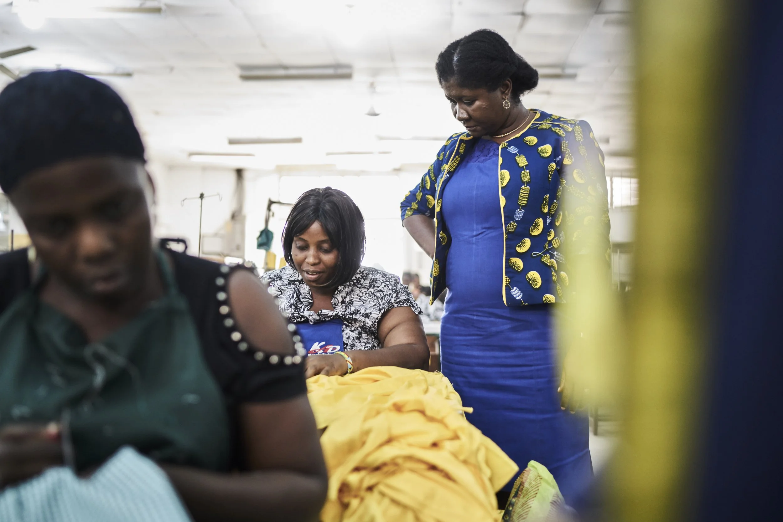 Award Winning Stanford Seed image: Three women working in a textile business in Africa, with fabric and sewing supplies around them.