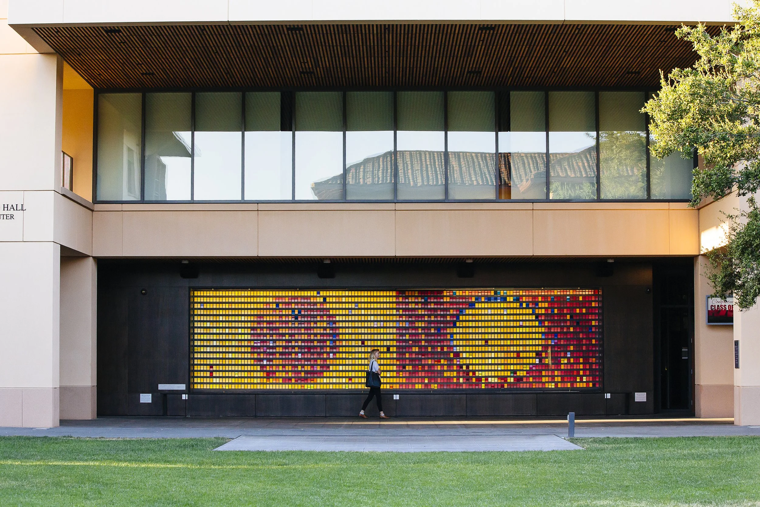 Campus beauty shot: located at Knight Management Center "Monument to Change as It Changes" kinetic art installation by artist Peter Wegner with student walking in front. Displaying two inverse circles in yellow and magenta.