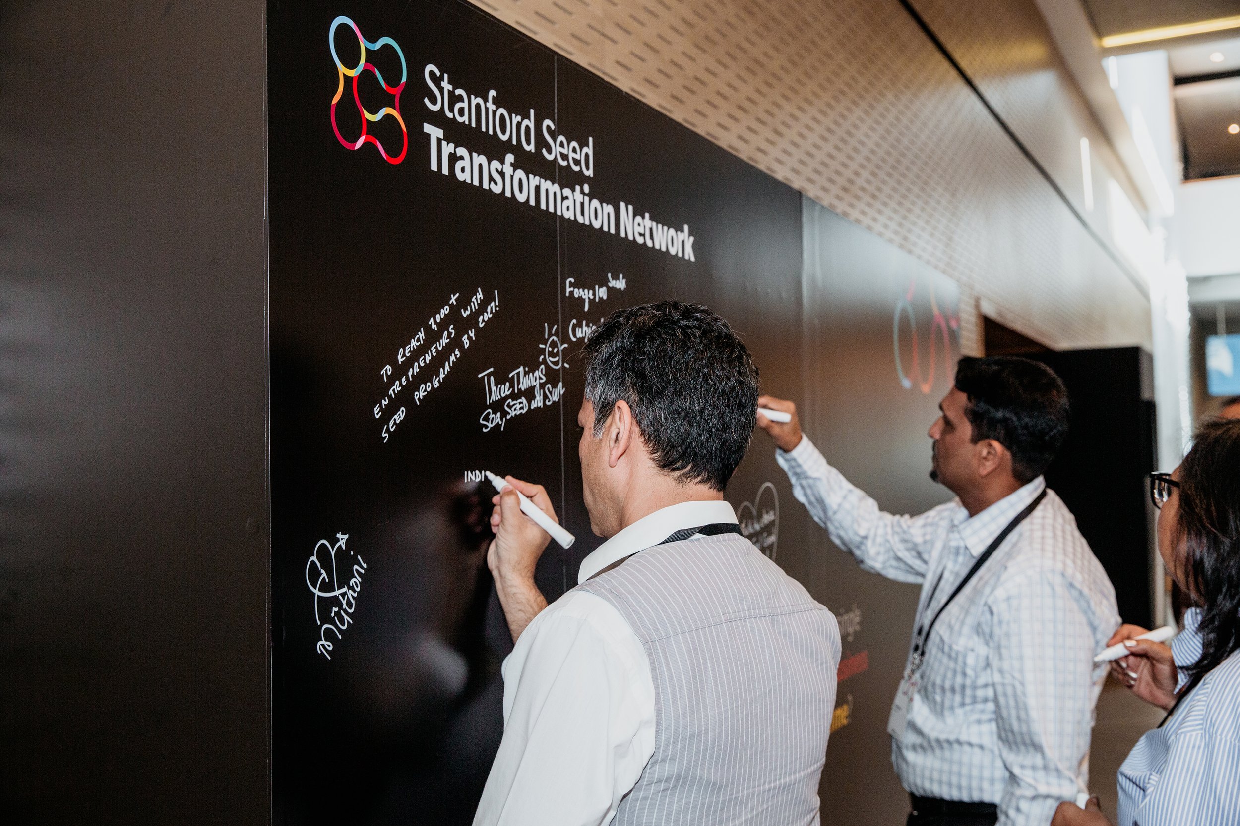 People writing on a blackboard with the title 'Stanford Seed Transformation Network'