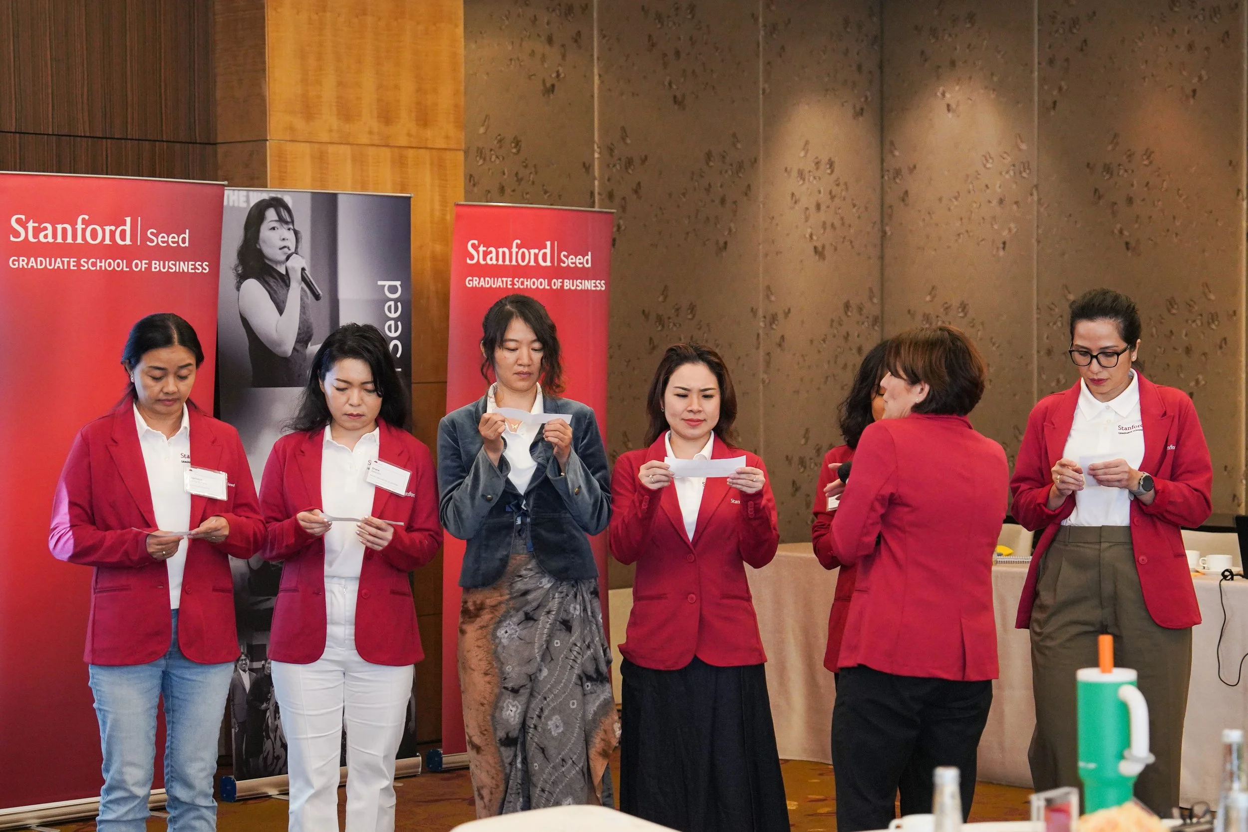Group of women in red blazers standing in front of Stanford Graduate School of Business banners during a Seed program.