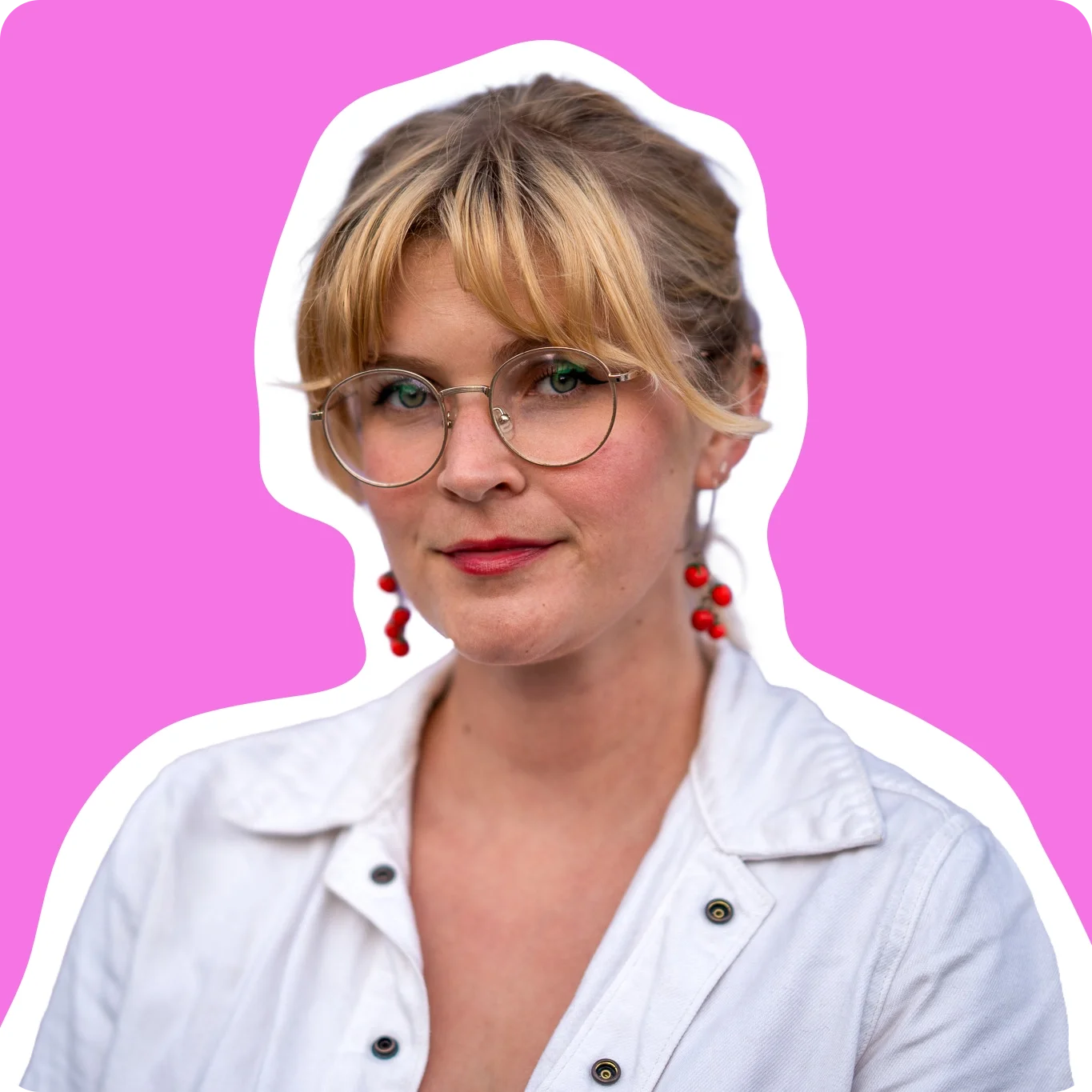Animator with short blonde hair, glasses, red lipstick, and red earrings, wearing a light-colored shirt with gold buttons, portrait against a bright pink-ish background.