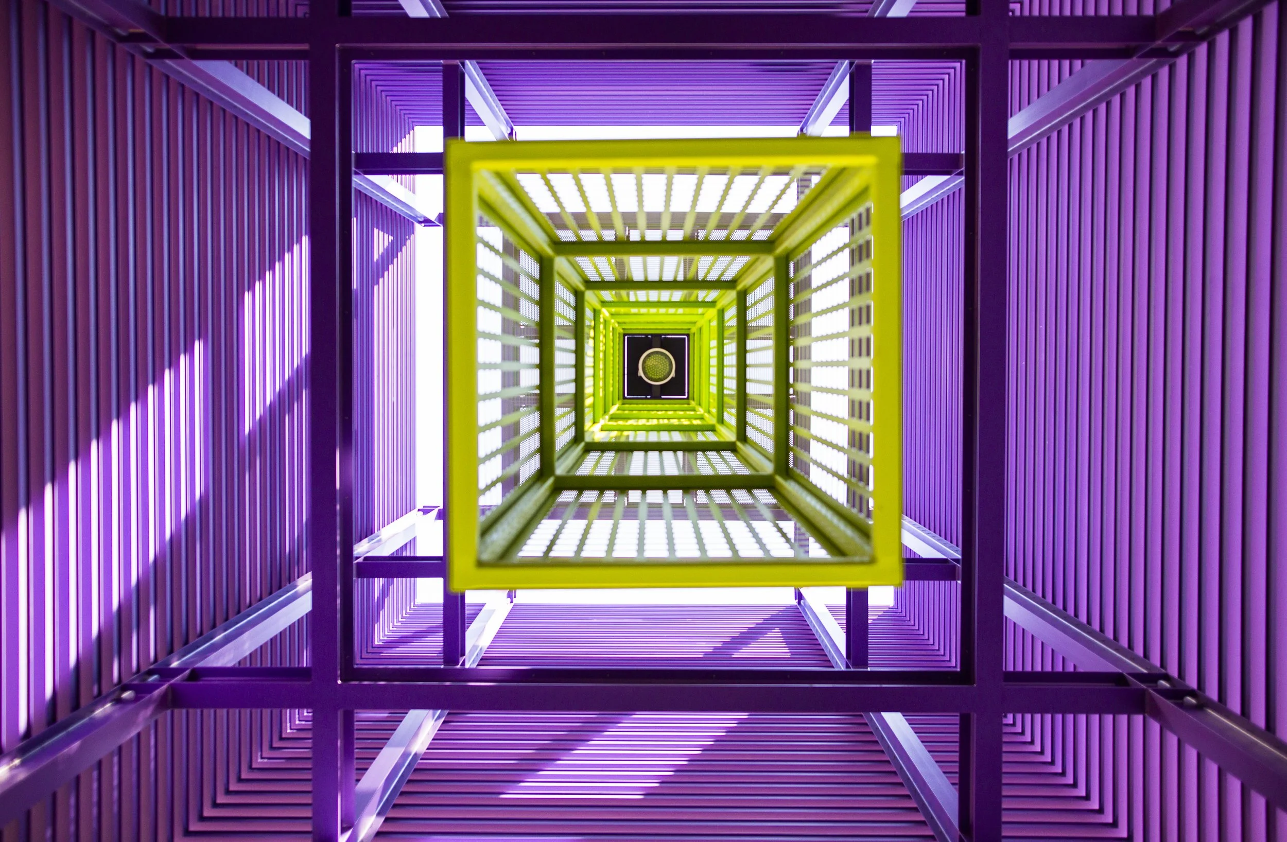 Stanford GSB brand refresh inspiration architecture image. Looking up at a colorful, modern staircase with rectangular frames in green and purple, viewed from the bottom of Highland Hall.