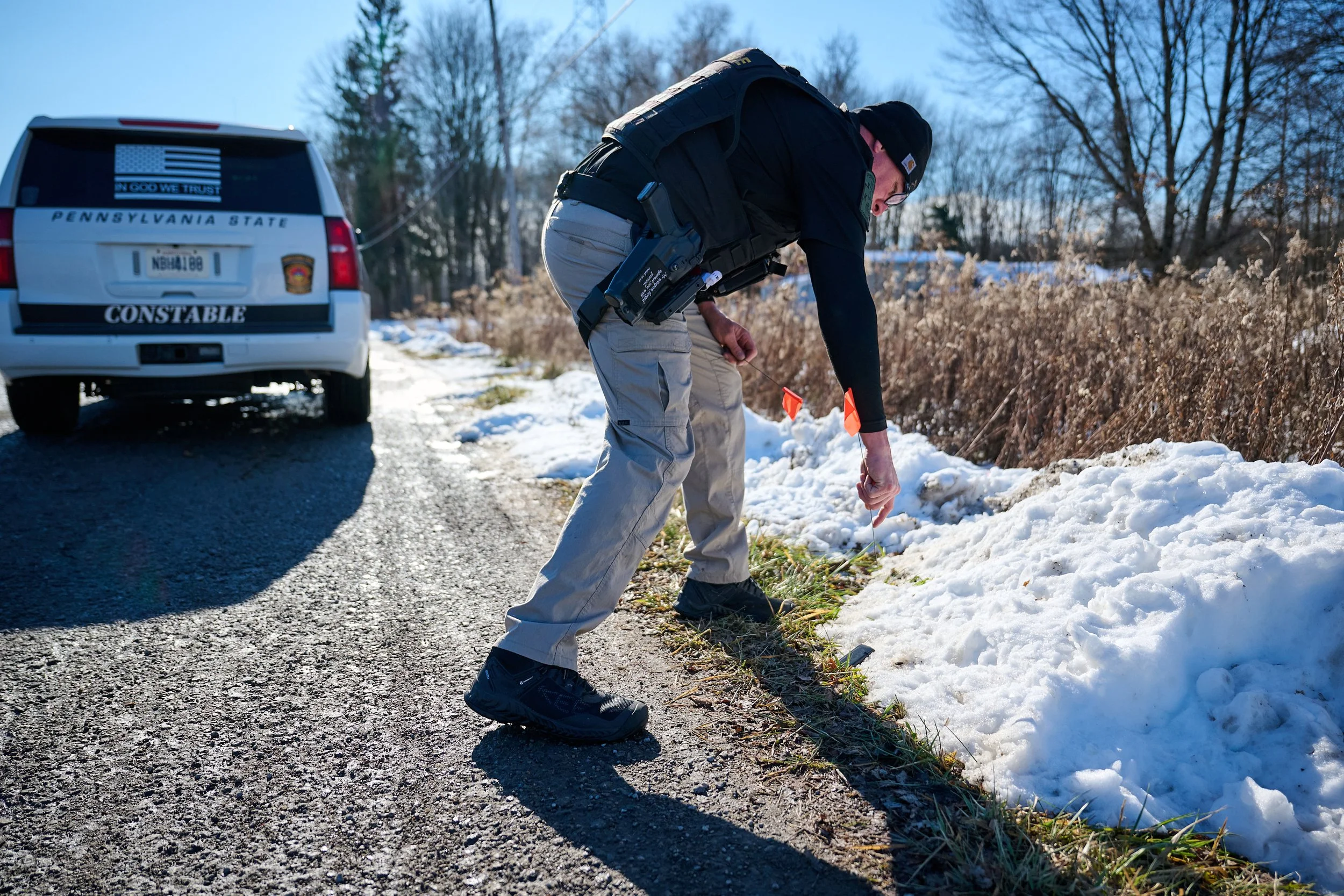 A law enforcement officer from Pennsylvania State Constable is marking location of a pistol magazine detected by the K-9 from the snow-covered roadside.
