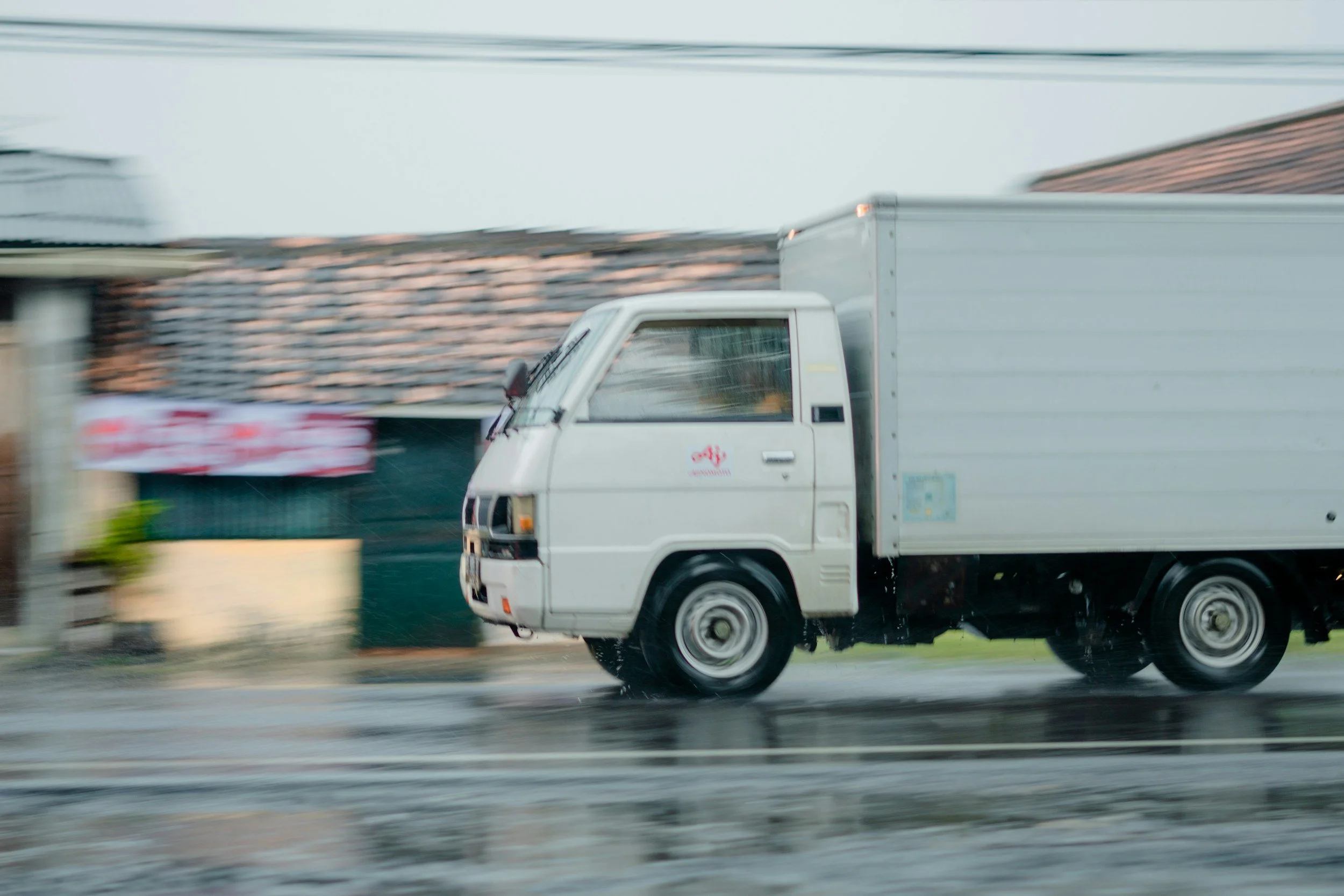 A small white delivery truck driving on a wet road during rain in Gibsonia, PA
