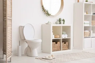 Minimalist bathroom with white toilet, wicker baskets, and open shelving unit with towels and decor, in a bright space with natural light.