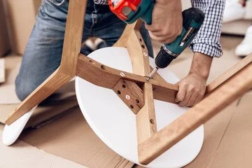 Person using a drill to assemble a wooden chair.
