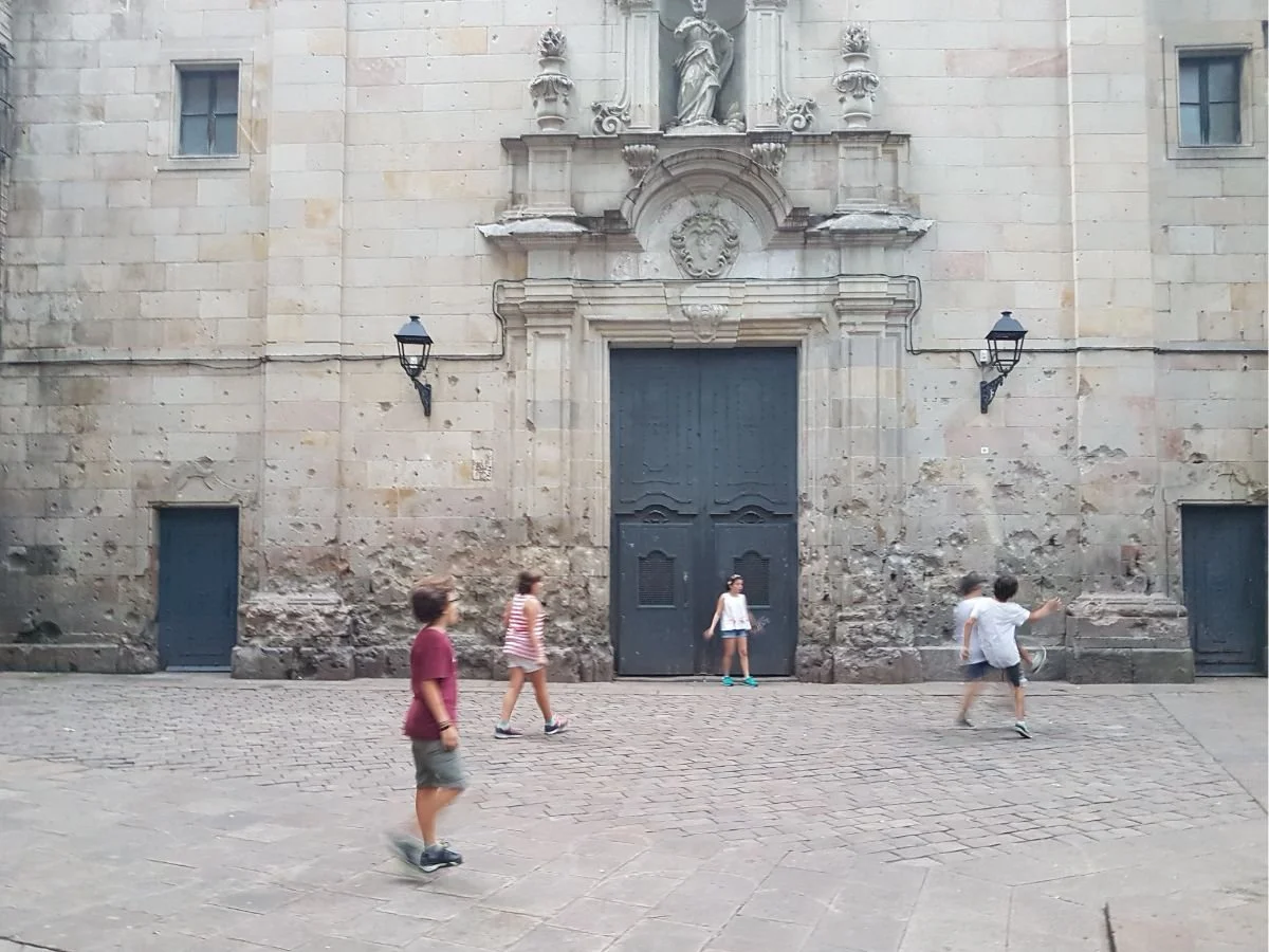 Plaça de Sant Felip Neri - skolebørn spiller bold foran kirken med dens hullede facade