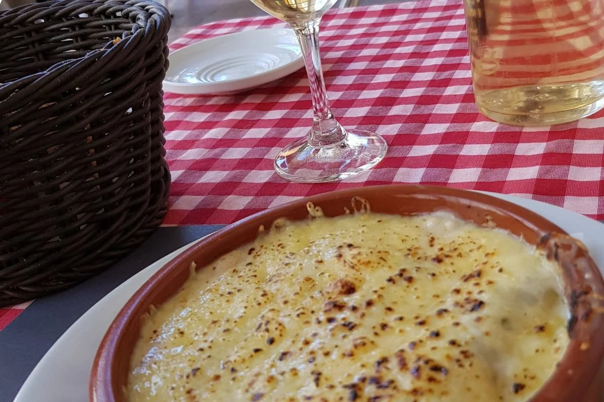 Gratinerede canelons serveret med et glas hvidvin på en restaurant i Barcelona
