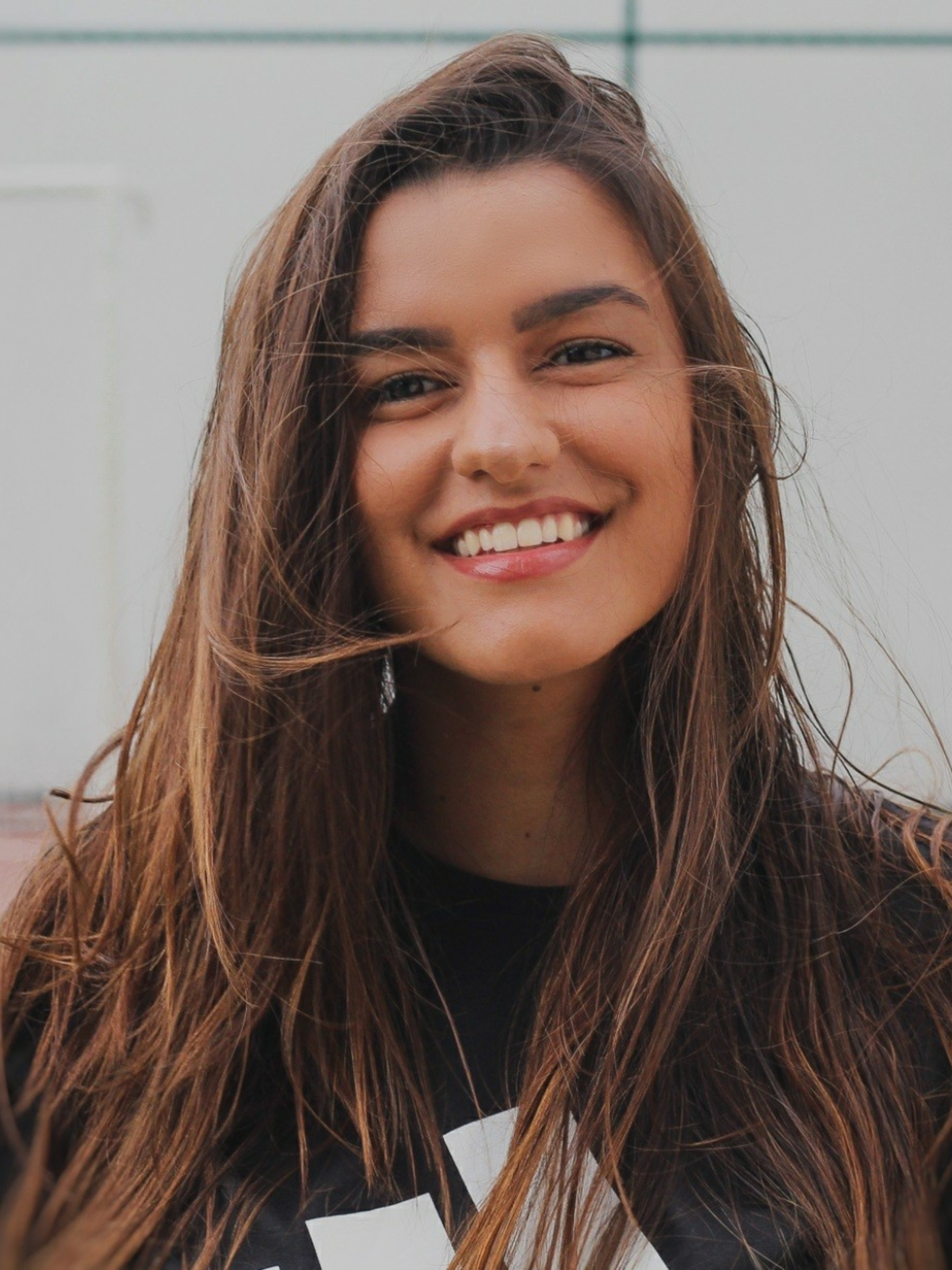 Close-up of a smiling woman with long brown hair, outside in front of a neutral background.