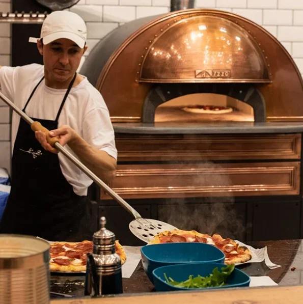 Pizzabäcker backt Pizza im Holzkohleofen in einer Pizzeria.