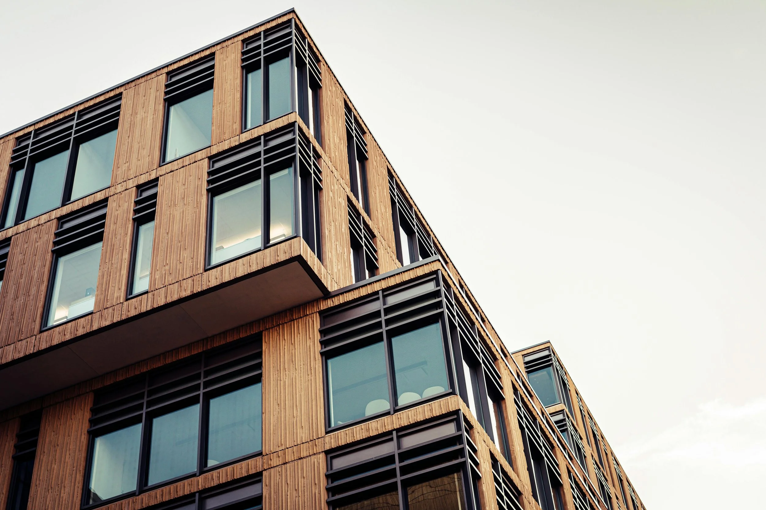 Modern wooden building with large glass windows and metal accents against a clear sky.