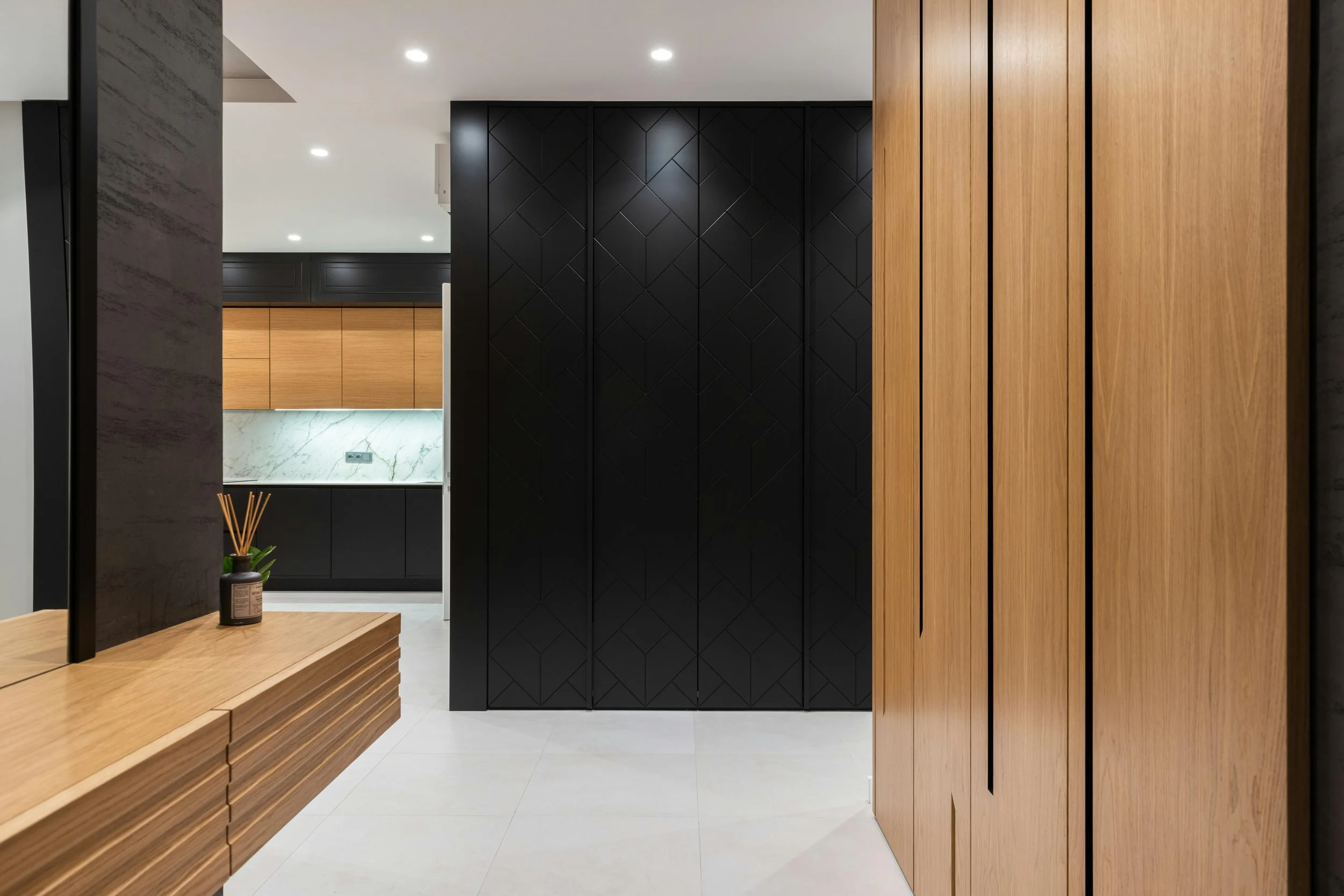 Modern interior with black and wood-paneled walls, a marble backsplash, wooden cabinetry, and a small table with a diffuser and plant.