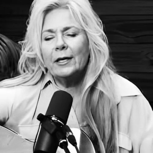 A woman with long, wavy hair singing or speaking into a microphone during a performance or recording session.