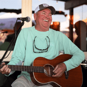 Man playing guitar and singing at an outdoor event, smiling.