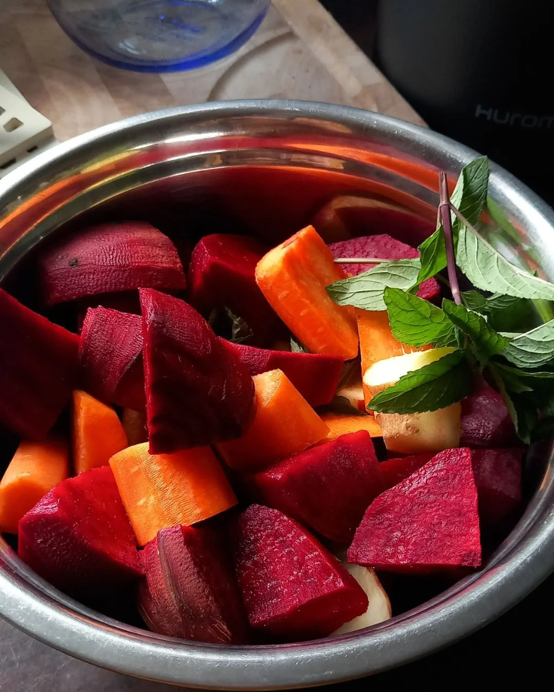 A bowl containing chopped red beets, carrots, and additional root vegetables, garnished with fresh mint leaves.