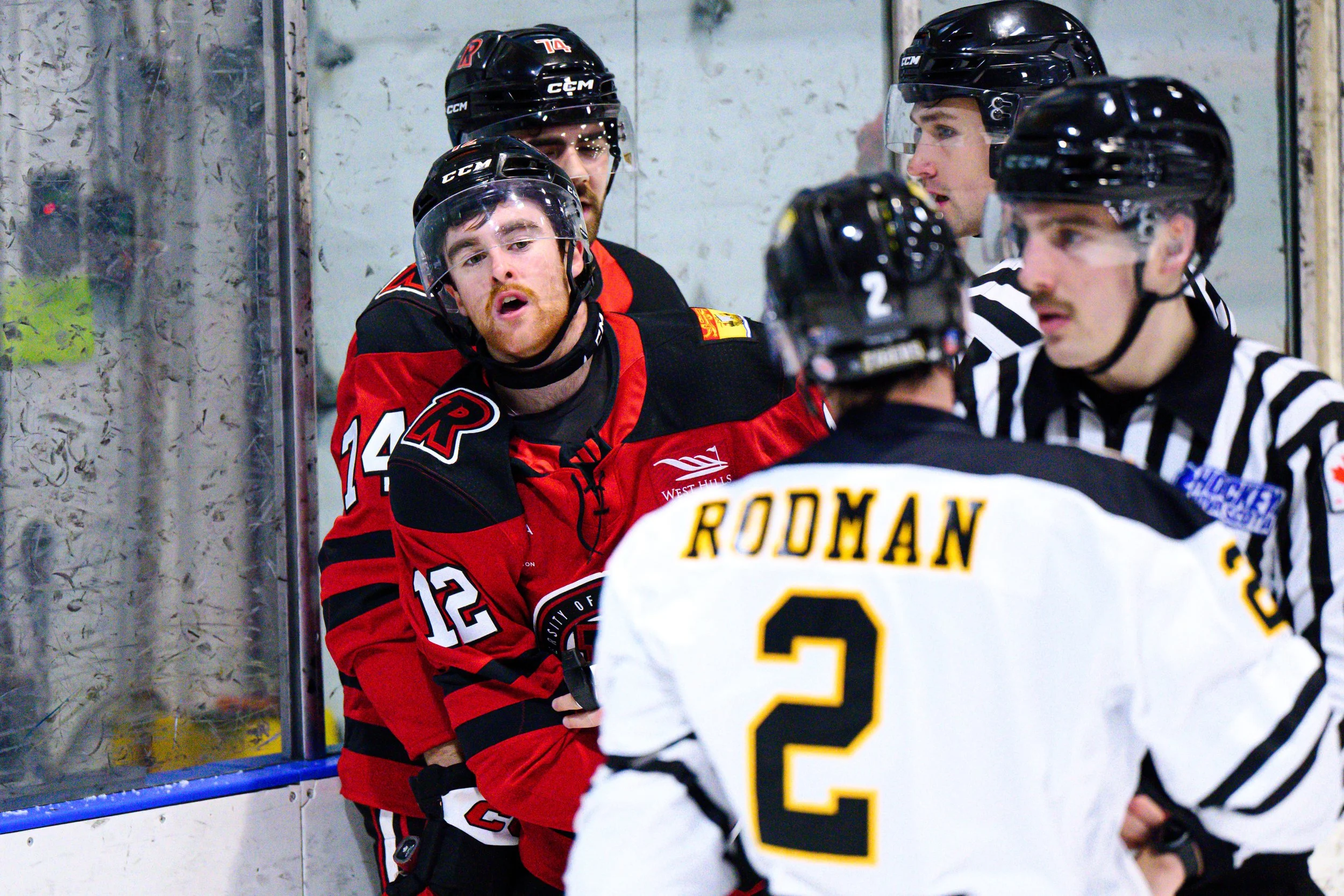Hockey players in helmets and jerseys arguing and arguing with each other and a referee during a game at the rink.