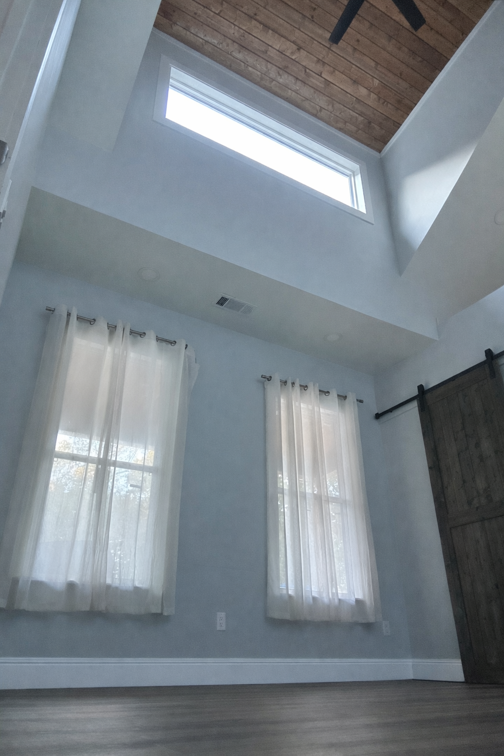 Room interior with high ceiling, skylight, two windows with white curtains, and wooden sliding door.