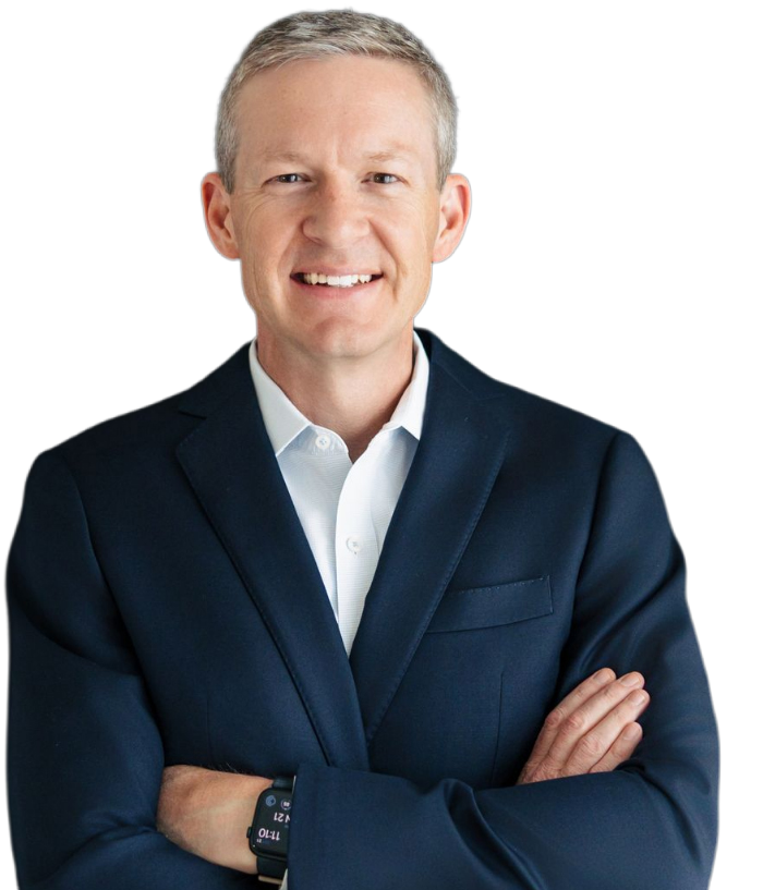 A smiling middle-aged man with short gray hair, wearing a navy blue suit and white dress shirt, standing with his arms crossed.