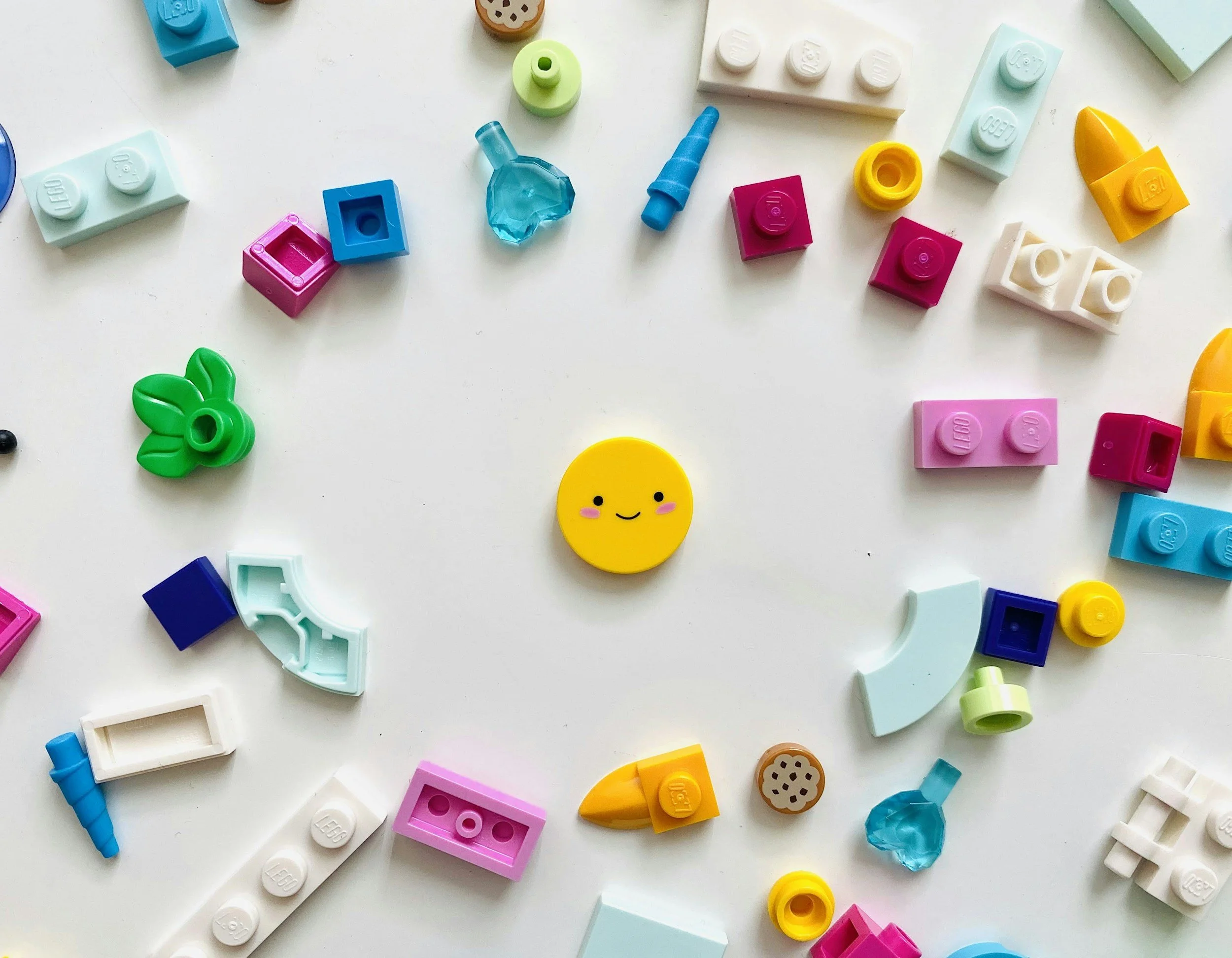 Colorful toy building blocks and a small round yellow smiling face on a white surface.